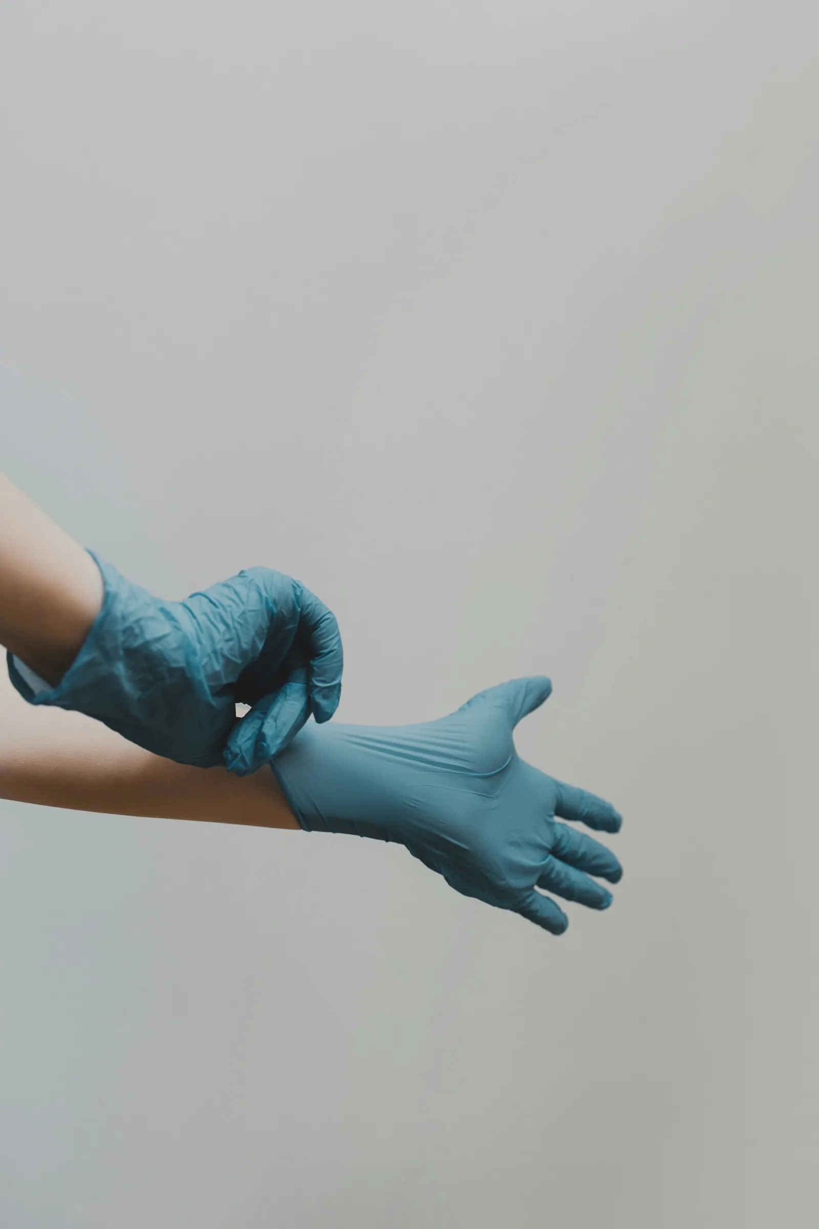 Mãos calçando uma luva médica azul sobre fundo neutro